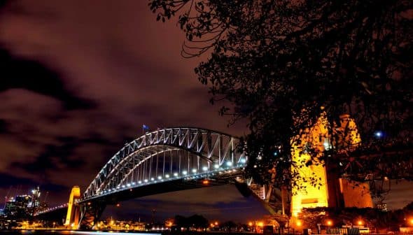 Sydney Harbour Bridge illuminated at night with a clear sky and clouds in the background. - Olive Oil Times