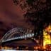 Sydney Harbour Bridge illuminated at night with a clear sky and clouds in the background. - Olive Oil Times