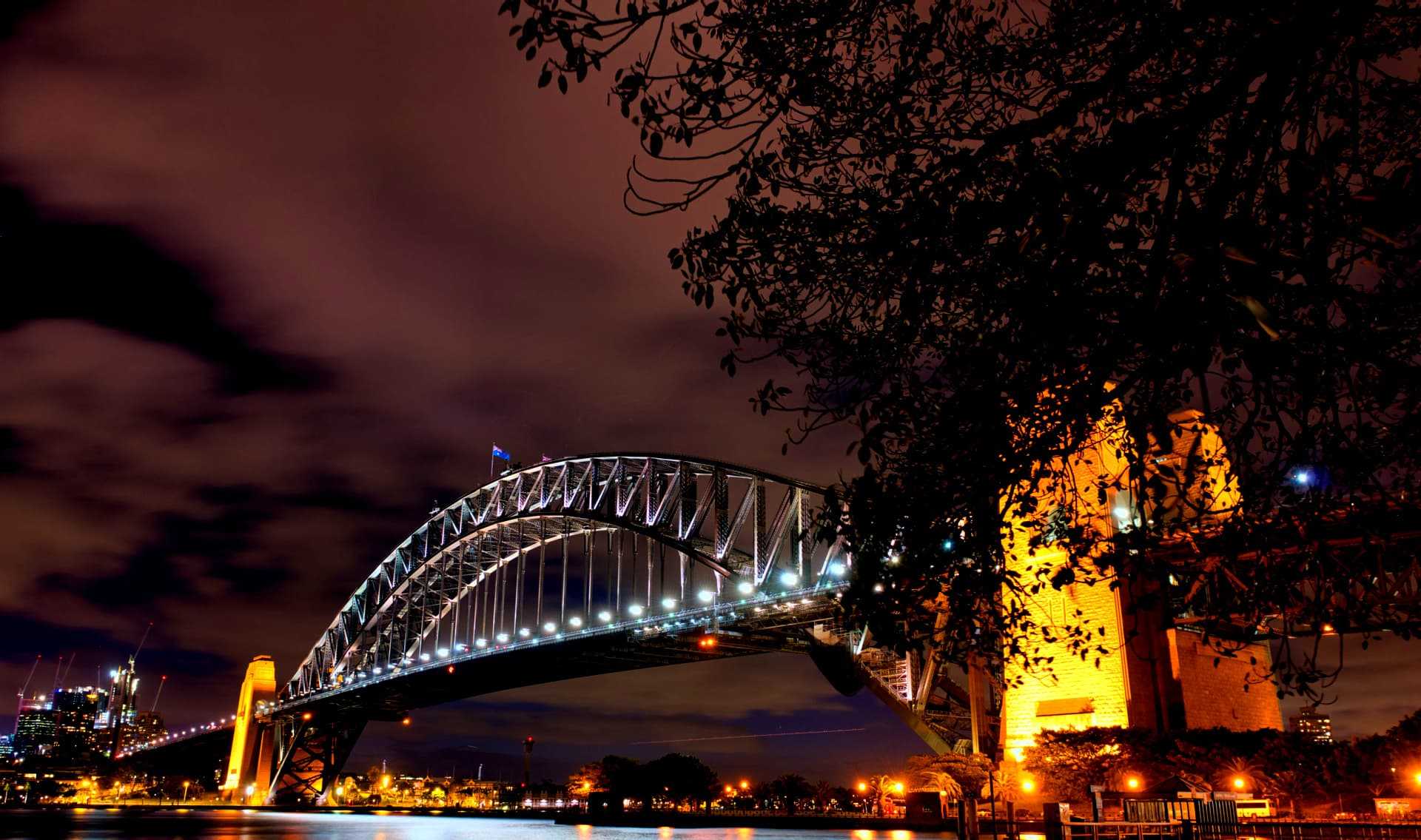 Sydney Harbour Bridge illuminated at night with a clear sky and clouds in the background. - Olive Oil Times