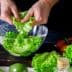 Person tearing fresh green lettuce leaves into a glass bowl for salad preparation. - Olive Oil Times