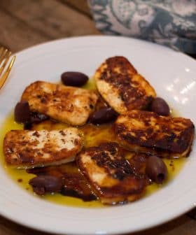 Plate of fried halloumi cheese slices served with black olives and olive oil. - Olive Oil Times