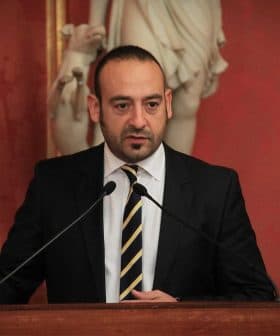 A man in a black suit speaking at a podium with two microphones in front of him. - Olive Oil Times