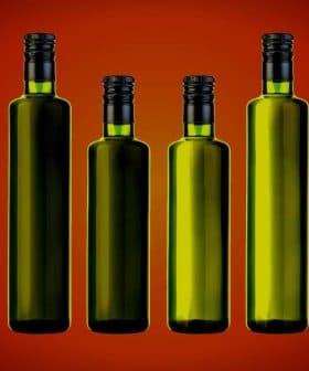 Eight green glass bottles with black caps arranged in a row against a gradient background. - Olive Oil Times