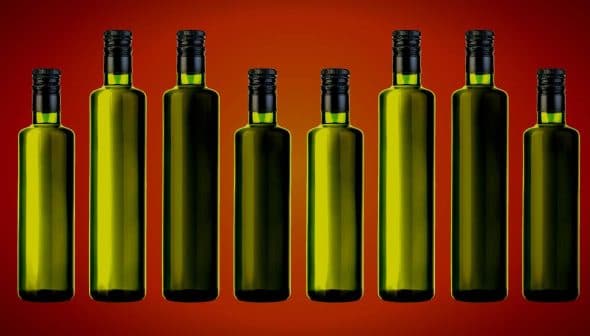 Eight green glass bottles with black caps arranged in a row against a gradient background. - Olive Oil Times