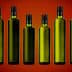 Eight green glass bottles with black caps arranged in a row against a gradient background. - Olive Oil Times