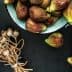A bowl filled with fresh figs alongside a bundle of dried poppy seed pods on a dark surface. - Olive Oil Times