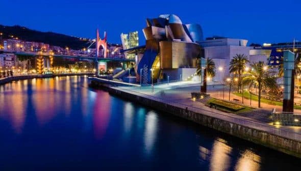 Guggenheim Museum in Bilbao illuminated at night with reflections in the water. - Olive Oil Times