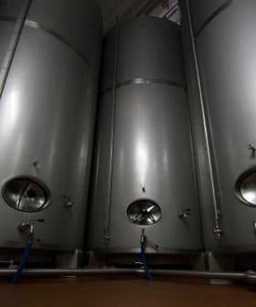 Three stainless steel storage tanks with valves and pipes in a facility. - Olive Oil Times