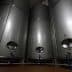 Three stainless steel storage tanks with valves and pipes in a facility. - Olive Oil Times