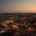 A panoramic view of Lisbon cityscape at dusk with lights illuminating the buildings and the bridge in the background. - Olive Oil Times