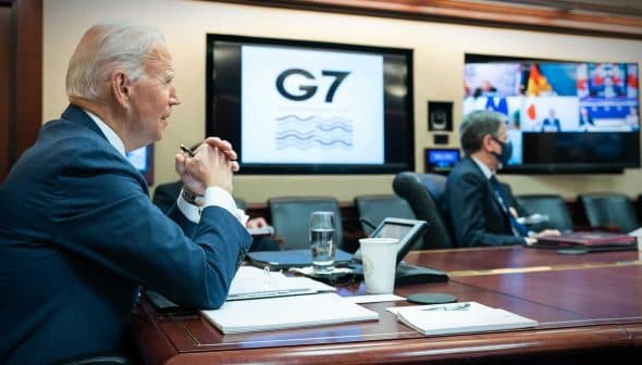 Joe Biden seated at a conference table during a G7 meeting with screens displaying participants. - Olive Oil Times