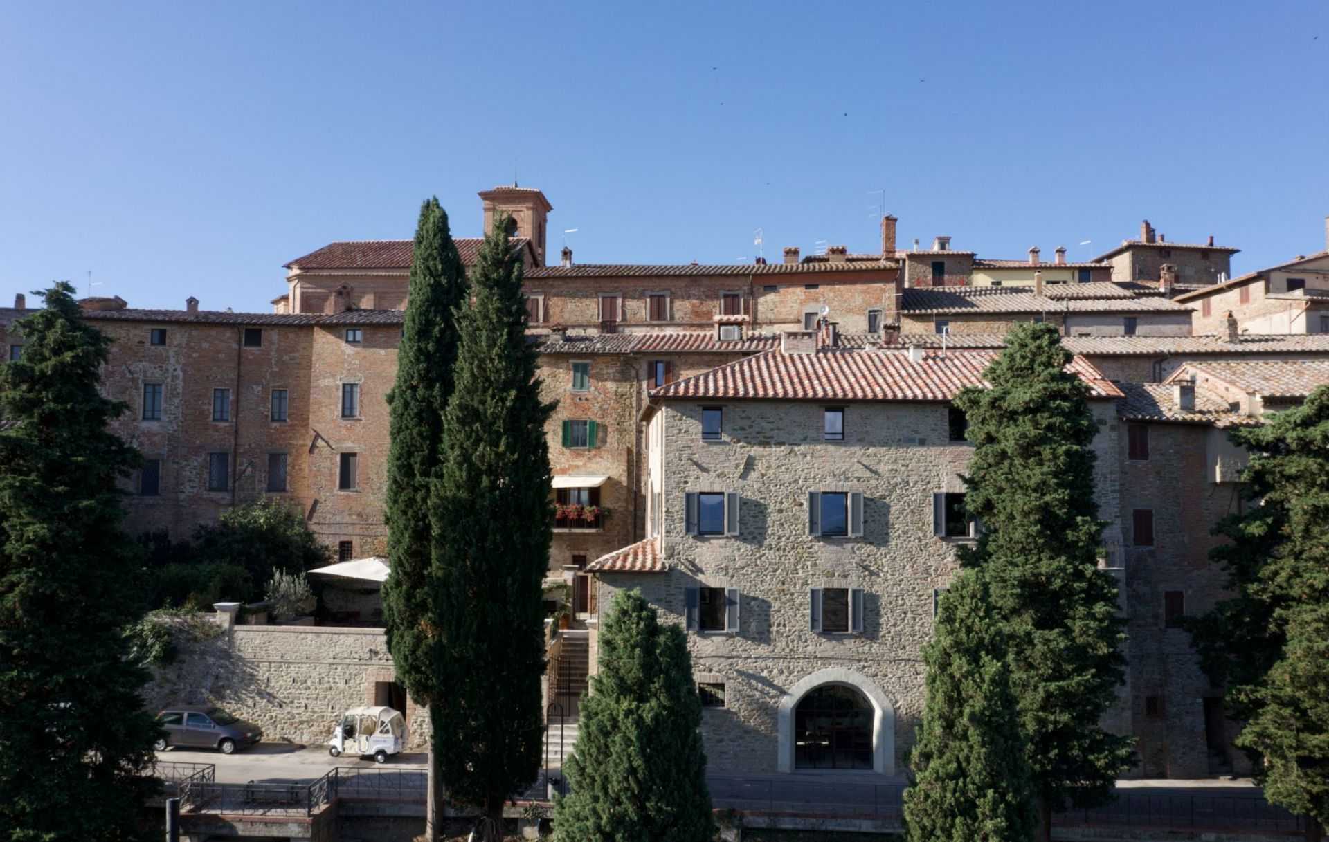 Stone buildings with terracotta roofs in a Tuscan village, surrounded by tall trees. - Olive Oil Times