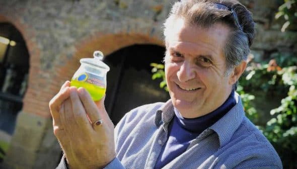Man smiling while holding a small jar of green olive oil in his hand. - Olive Oil Times