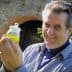 Man smiling while holding a small jar of green olive oil in his hand. - Olive Oil Times