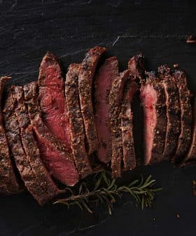 Sliced roast beef arranged on a slate surface with herbs. - Olive Oil Times