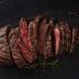 Sliced roast beef arranged on a slate surface with herbs. - Olive Oil Times