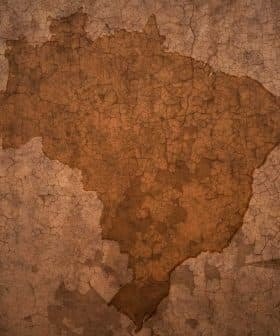 Silhouette map of Brazil displayed on a textured, cracked brown background. - Olive Oil Times