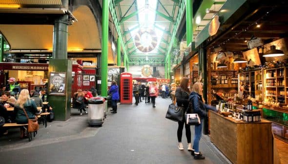 Interior view of a market featuring various stalls and shoppers walking through the aisles. - Olive Oil Times
