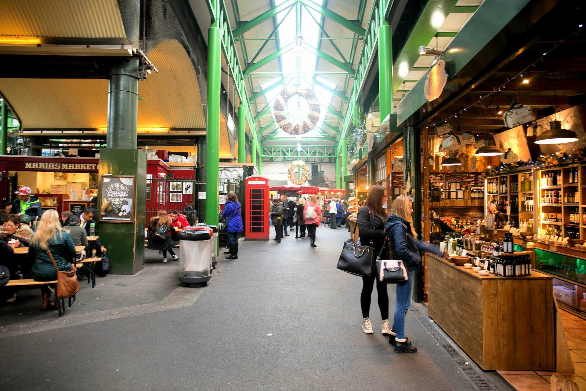 Interior view of a market featuring various stalls and shoppers walking through the aisles. - Olive Oil Times