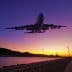 An airplane flying above a river during sunset with wind turbines in the background. - Olive Oil Times
