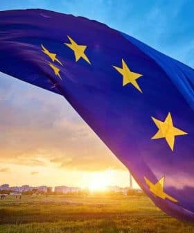European Union flag with stars waving against a sunset sky with clouds. - Olive Oil Times