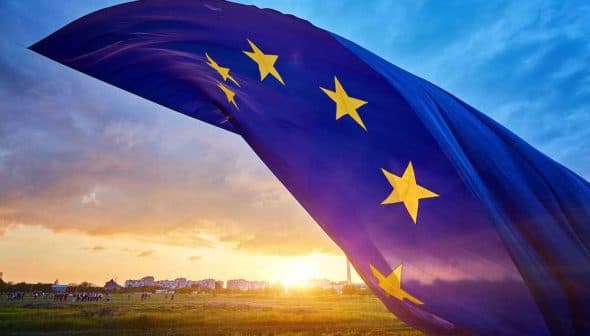 European Union flag with stars waving against a sunset sky with clouds. - Olive Oil Times