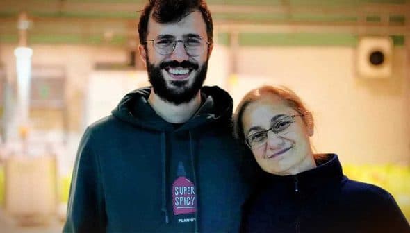 A man and a woman smiling while standing close to each other in a well-lit indoor setting. - Olive Oil Times