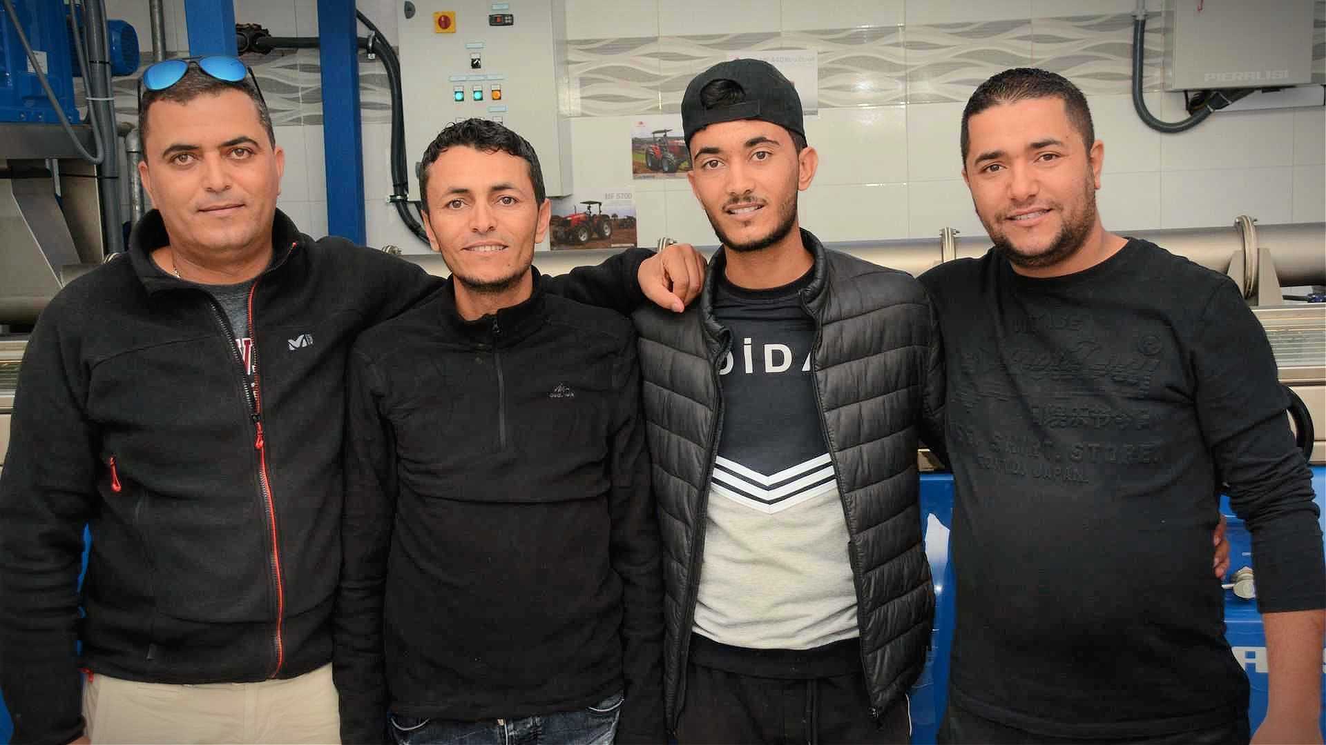 Four men wearing black clothing posing together in a casual setting. - Olive Oil Times