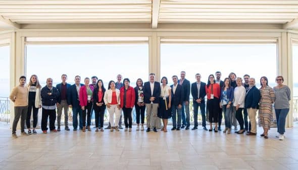 A group of individuals posing for a photo at an event, standing together in a spacious indoor area. - Olive Oil Times