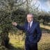 A man in a suit standing beside an olive tree in an outdoor setting. - Olive Oil Times