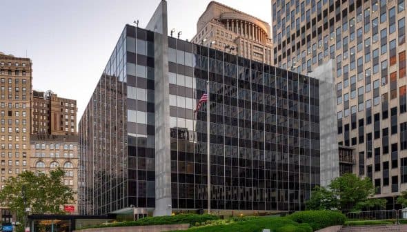 Contemporary office building featuring a glass facade and surrounding greenery in an urban setting. - Olive Oil Times