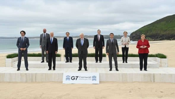 Group photo of G7 leaders standing on a stage at a beach in Cornwall. - Olive Oil Times