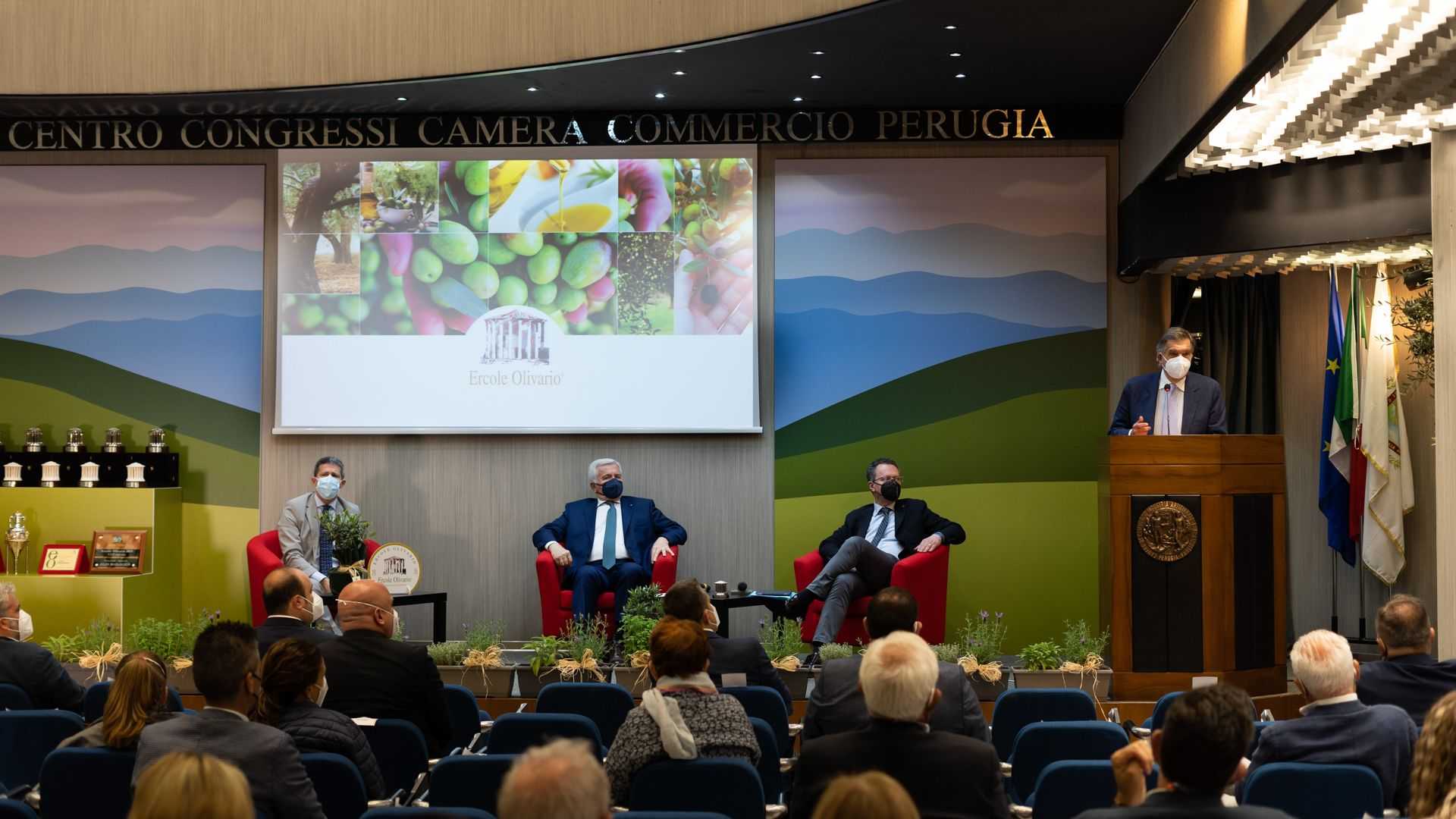 Panel discussion featuring three seated speakers and one speaker at a podium during the Ercole Olivario event. - Olive Oil Times
