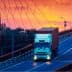 A white truck with a container driving on a bridge during sunset with colorful sky. - Olive Oil Times
