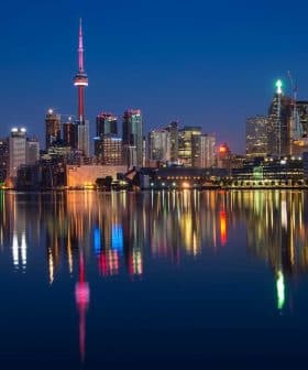 Toronto city skyline featuring the CN Tower and illuminated buildings reflected in water at night. - Olive Oil Times