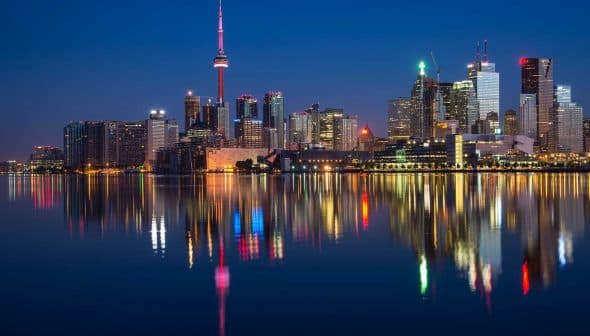 Toronto city skyline featuring the CN Tower and illuminated buildings reflected in water at night. - Olive Oil Times