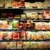 Various packaged food items displayed on a grocery store shelf, including meats and snacks. - Olive Oil Times