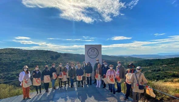 A group of individuals standing together outdoors, wearing bags and posing for a photo in a natural setting. - Olive Oil Times