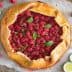 A raspberry galette topped with fresh mint leaves and lime slices on a baking sheet. - Olive Oil Times