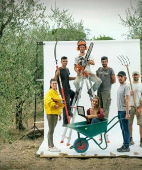Group of six individuals posing with various gardening tools in an olive grove setting. - Olive Oil Times