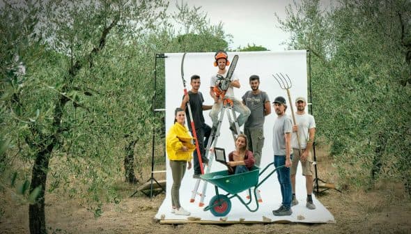 Group of six individuals posing with various gardening tools in an olive grove setting. - Olive Oil Times