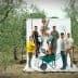 Group of six individuals posing with various gardening tools in an olive grove setting. - Olive Oil Times