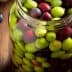 Glass jar filled with a mix of green and black olives on a wooden surface. - Olive Oil Times