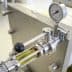 Close-up of oil filtration equipment showing a pressure gauge and transparent tube with liquid. - Olive Oil Times