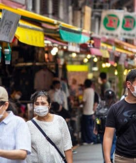 Group of people wearing face masks walking through a market with colorful awnings. - Olive Oil Times
