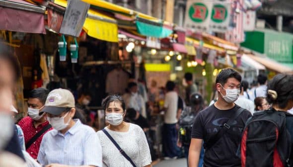 Group of people wearing face masks walking through a market with colorful awnings. - Olive Oil Times