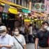 Group of people wearing face masks walking through a market with colorful awnings. - Olive Oil Times