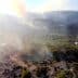 Aerial view of a landscape with smoke rising from the ground among trees and rocky terrain. - Olive Oil Times