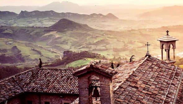 View of rooftops with a mountainous landscape in the background during sunset. - Olive Oil Times