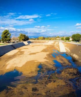 A dry riverbed with patches of water and sparse vegetation under a blue sky with clouds. - Olive Oil Times